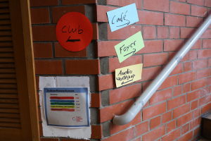 An einer Wand kleben verschiedene Wegweiser und Hinweisschilder