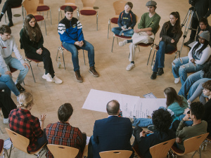 Jugendliche sitzen in einem Stuhlkreis und diskutieren mit dem OB Kandidaten, In der Mitte liegt ein großes weißes Plakat.