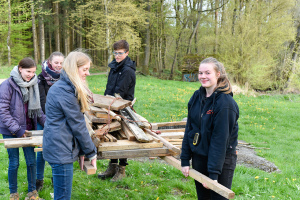 Jugendliche tragen zusammen eine Stapel mit Holz.