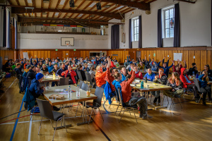 Viele junge Menschen sitzen bei einer Versammlung an Tischen und stimmen mit Handzeichen ab
