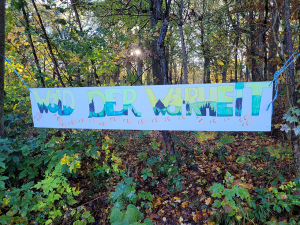 Ein Plakat hängt im Wald zwischen Bäumen. Darauf sthet Wald der Wahrheit.